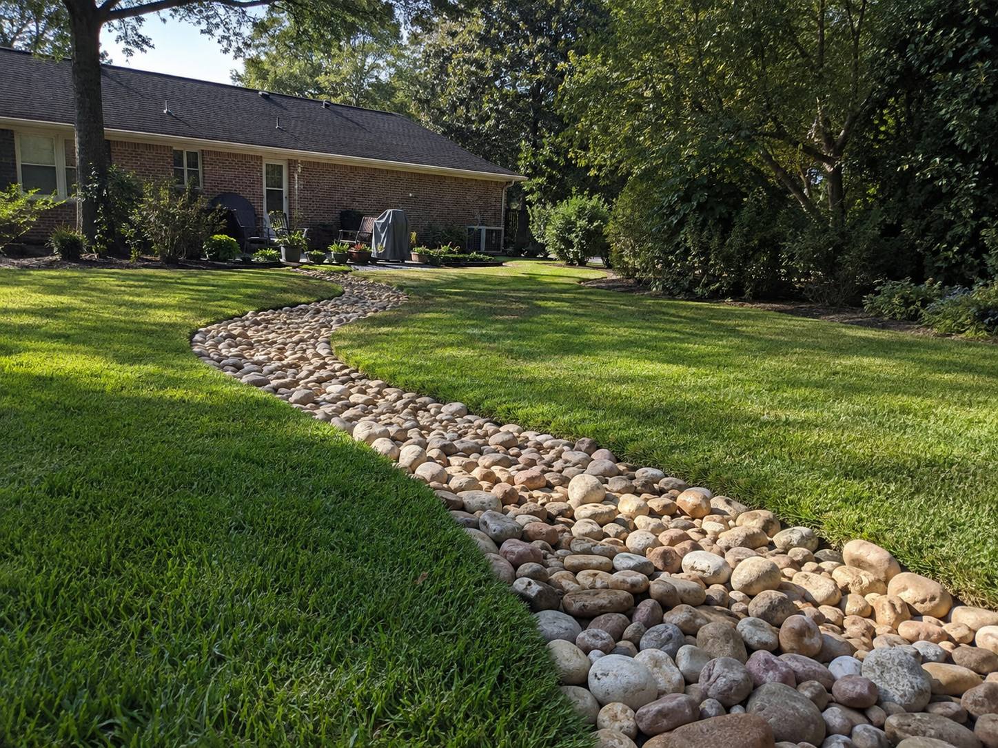 A river-rock dry creek bed curving through a green lawn, carrying runoff away from the house