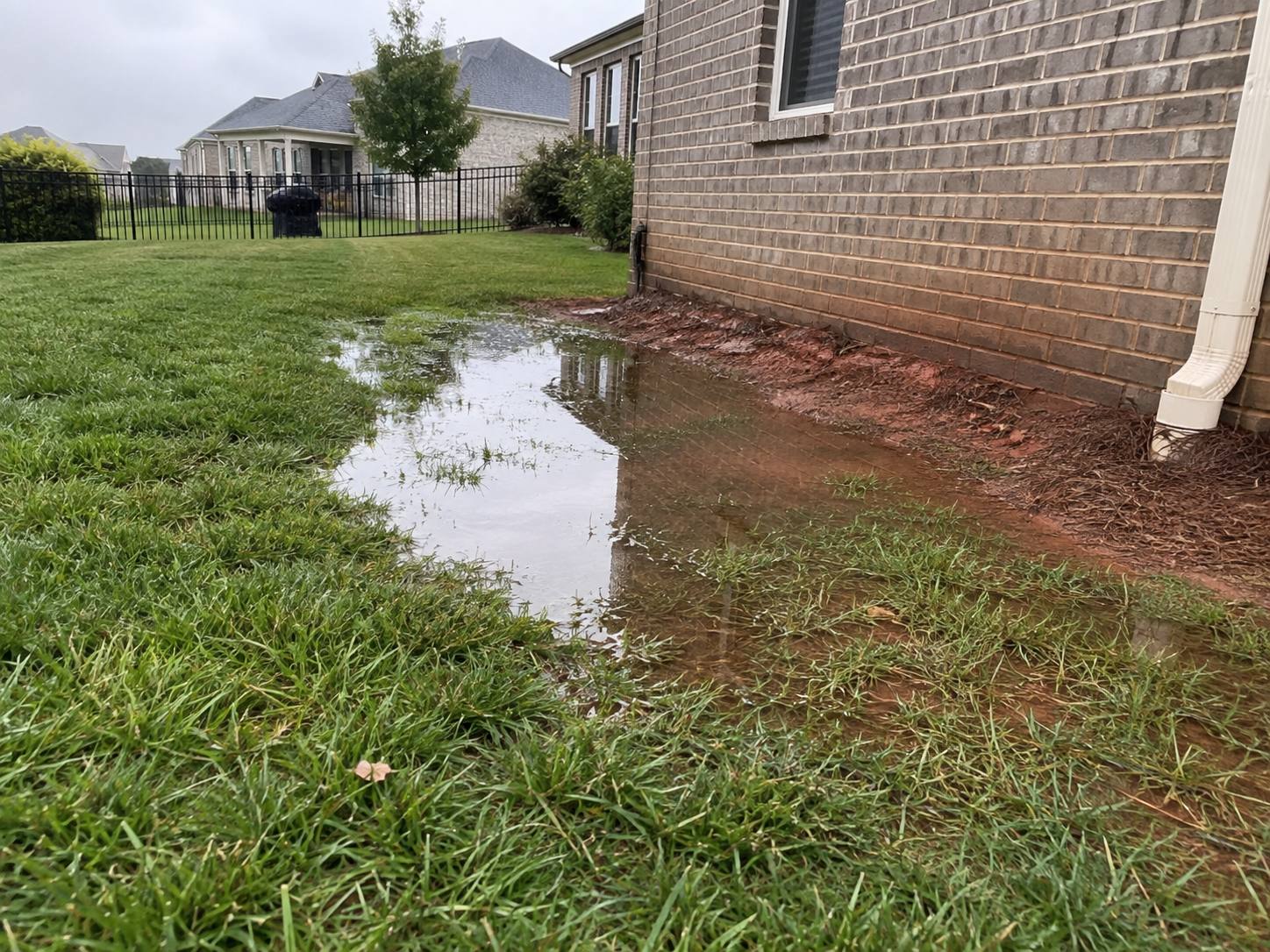 Rainwater pooled against a brick home's foundation where a downspout empties into the lawn