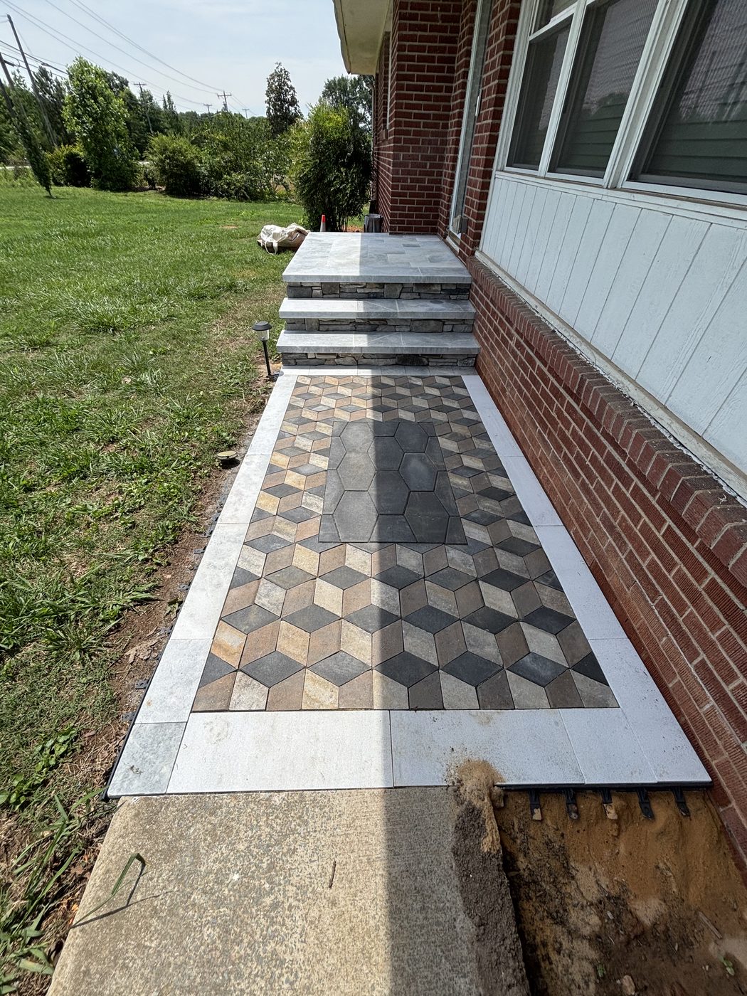 Front walkway in a three-dimensional cube paver pattern with a light stone border, leading to new stone-clad front steps of a brick home