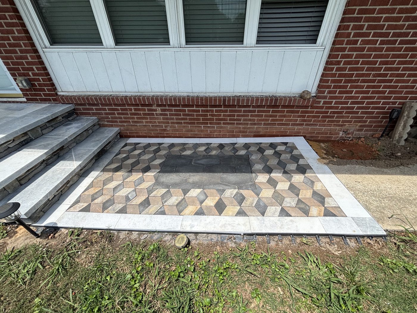 Paver walkway pad in a three-dimensional cube pattern with a hexagon center and light stone border, beside stone-clad front steps